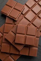 Photo of Delicious milk chocolate on black table, flat lay