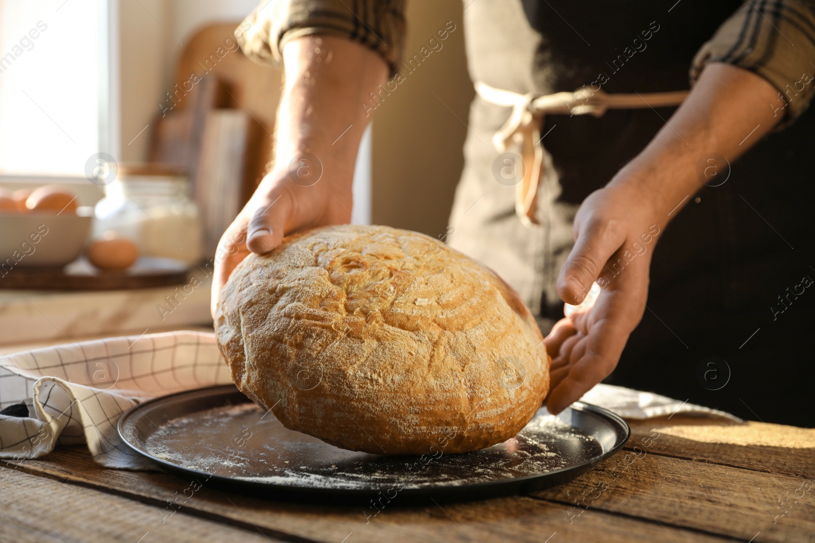 Photo of Man holding loaf of fresh bread at wooden table indoors, closeup