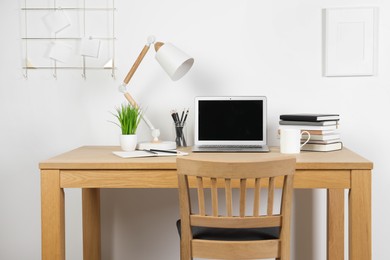 Cozy workspace with laptop, lamp and stationery on wooden desk at home