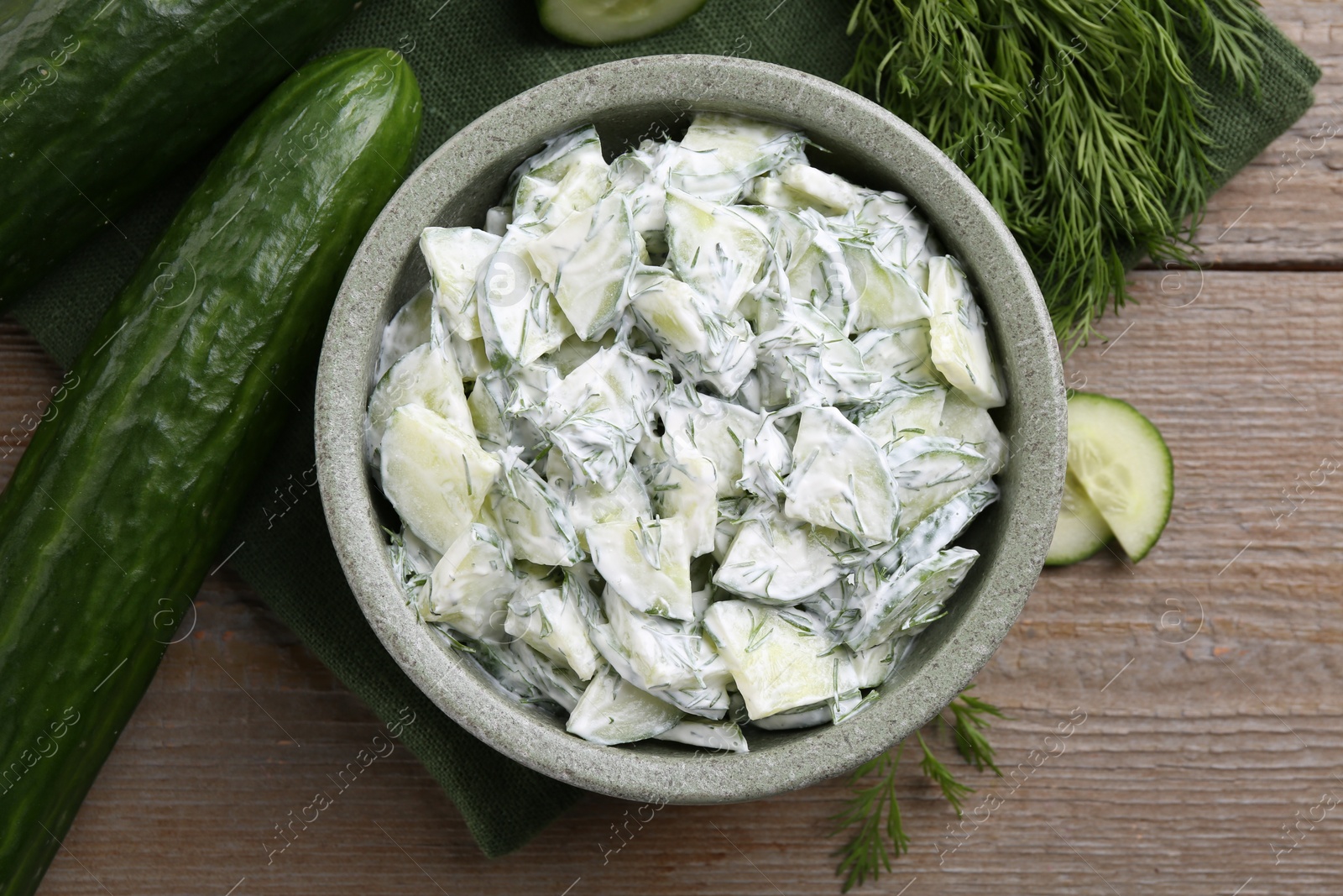Photo of Delicious cucumber salad in bowl and ingredients on wooden table, flat lay