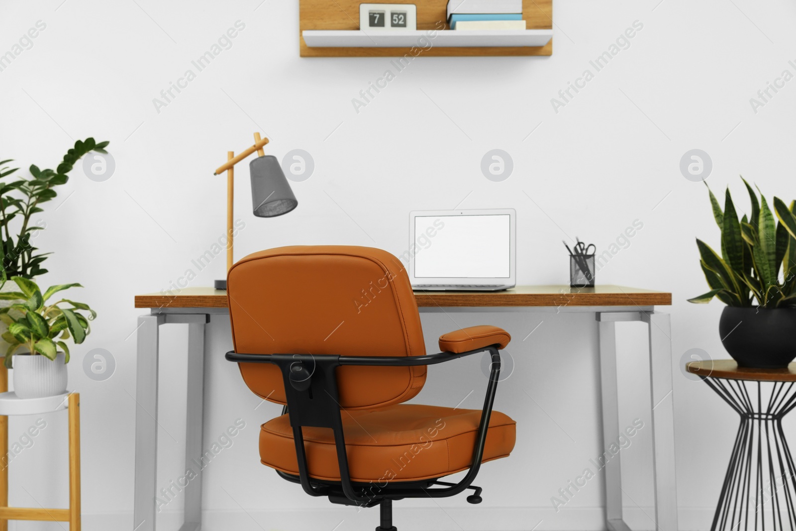 Photo of Stylish office interior with comfortable chair, desk, laptop and houseplants