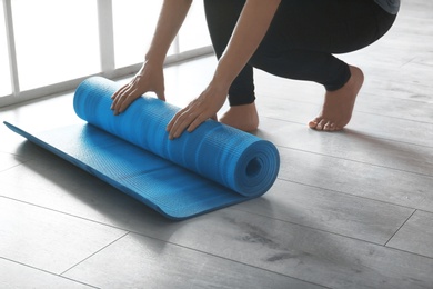 Photo of Woman rolling yoga mat on floor indoors, closeup