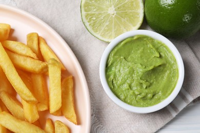 Photo of Plate with french fries, avocado dip and lime served on cloth, top view