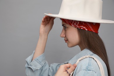 Photo of Young woman with hat and stylish bandana on grey background, closeup