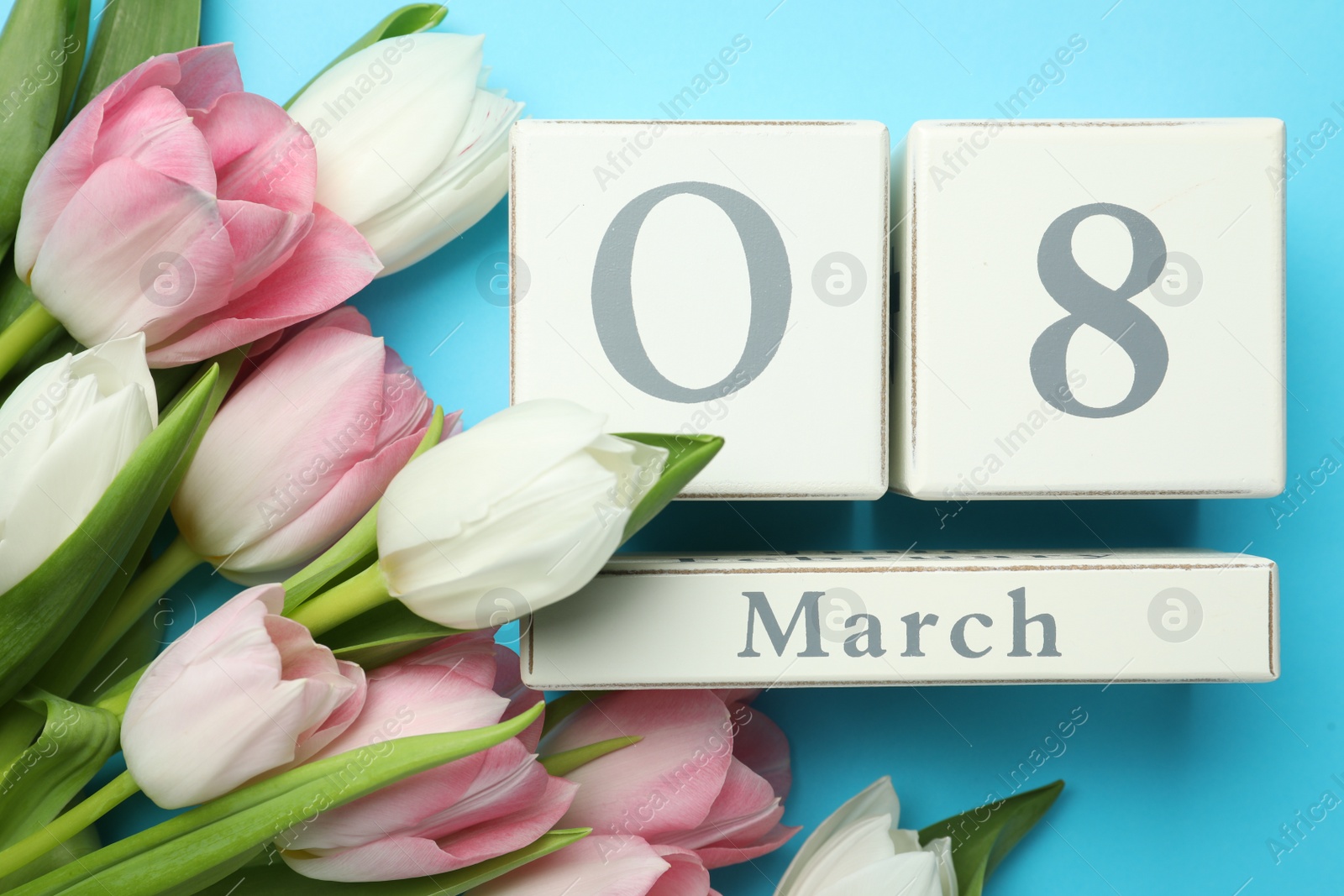Photo of Wooden block calendar with date 8th of March and tulips on light blue background, flat lay. International Women's Day