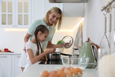Photo of Little girl with her mother cooking together in modern kitchen