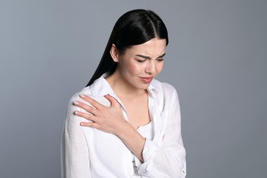 Woman suffering from shoulder pain on grey background