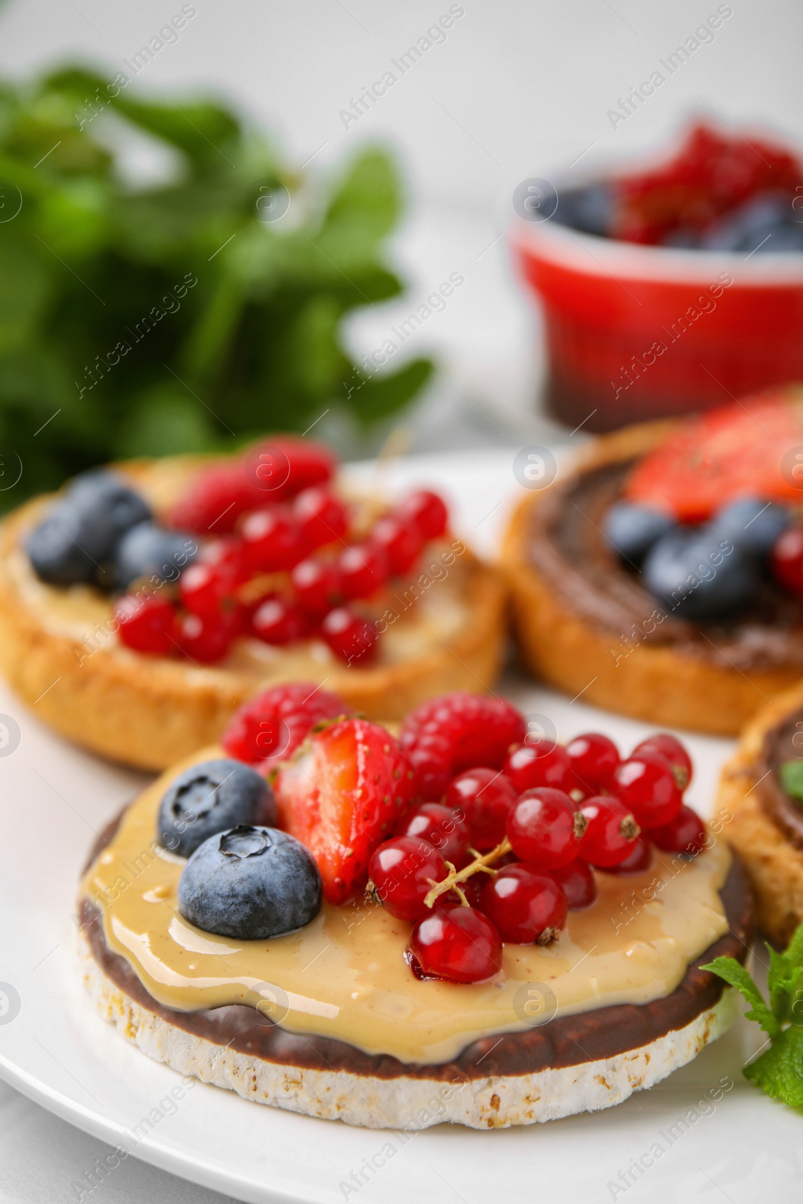 Photo of Fresh rice cake and rusks with different toppings served on white plate, closeup