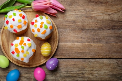 Photo of Traditional Easter cakes, tulips and colorful eggs on wooden table, flat lay. Space for text
