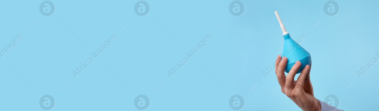 Photo of Man holding enema on light blue background, closeup