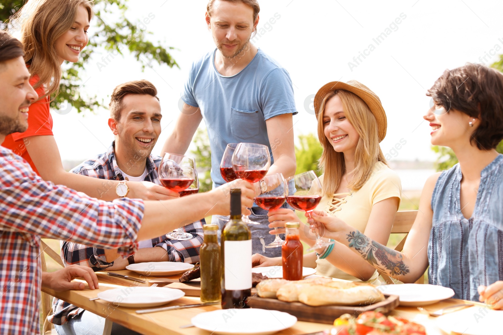 Photo of Young people with glasses of wine at table outdoors. Summer barbecue