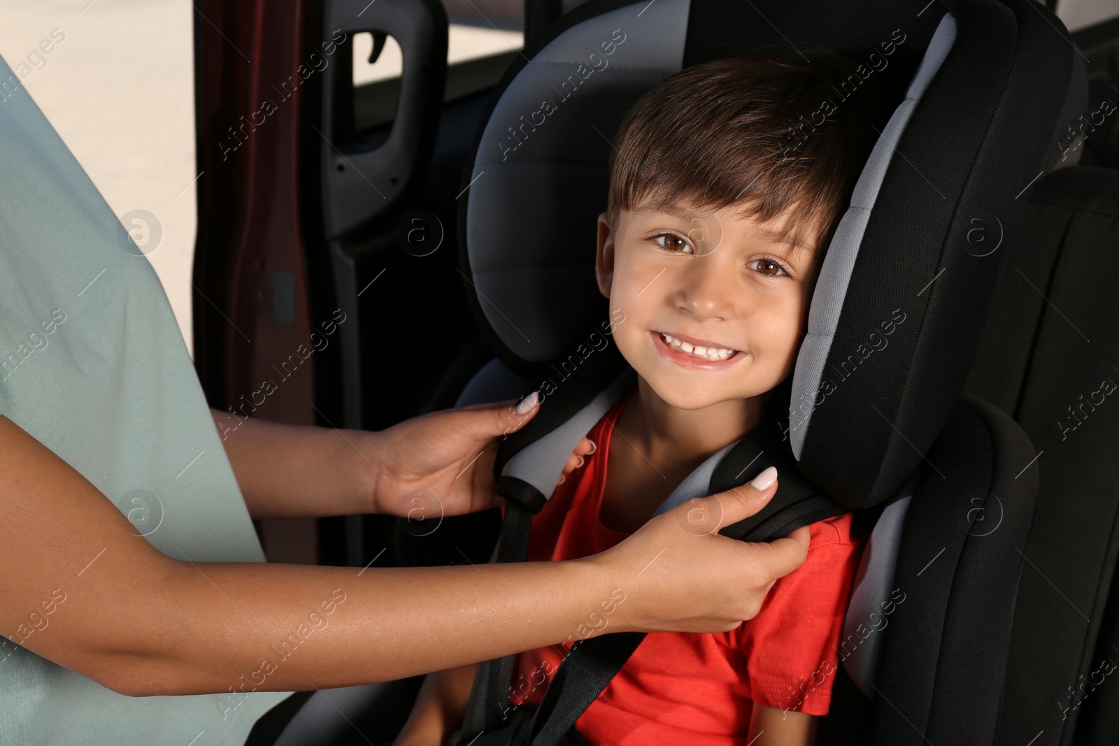 Photo of Mother fastening her son with car safety belt in child seat