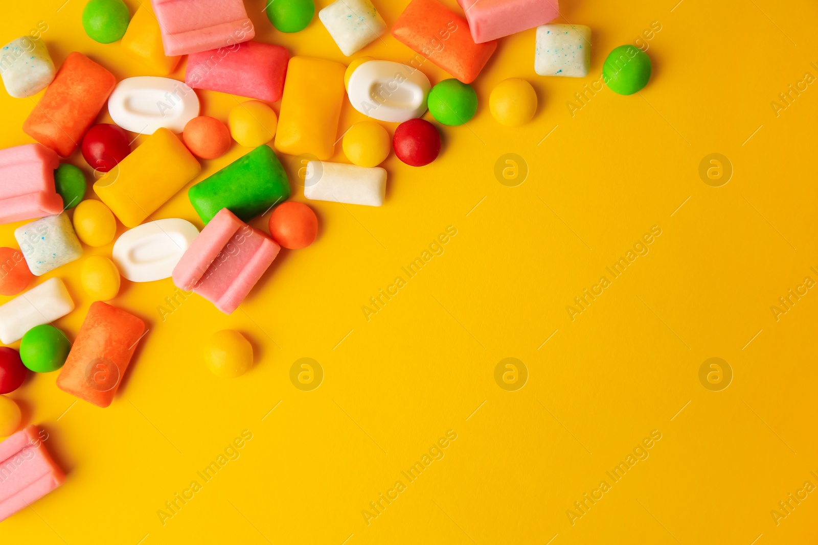 Photo of Many different chewing gums on yellow background, flat lay. Space for text