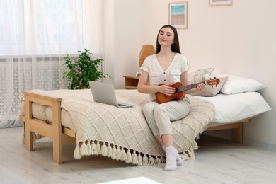 Photo of Woman learning to play ukulele with online music course at home. Space for text