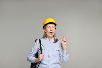 Photo of Architect in hard hat with tube pointing at something on grey background
