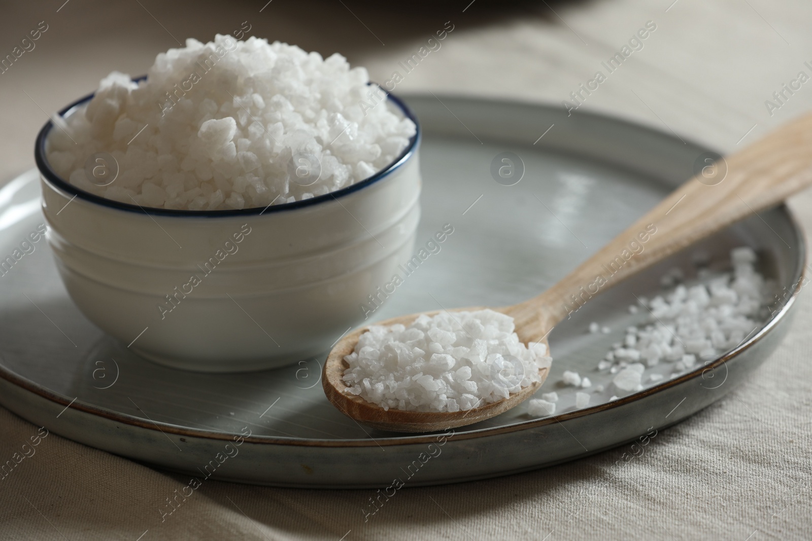 Photo of Organic salt in bowl and wooden spoon on table, closeup