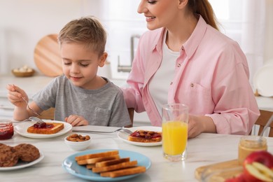 Photo of Mother and her cute little son having breakfast at table in kitchen, closeup