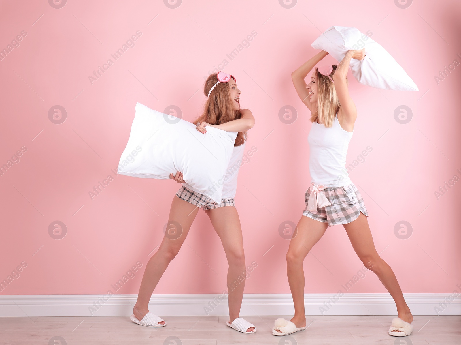 Photo of Two young women having pillow fight near color wall