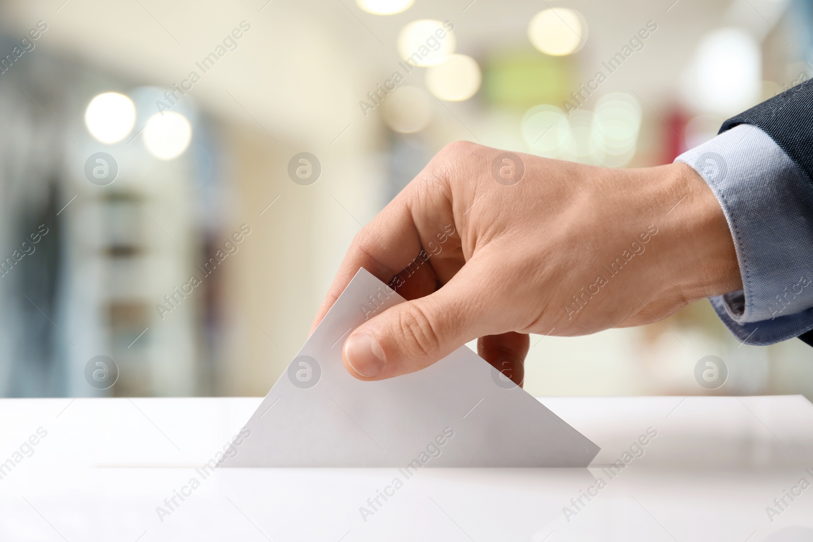 Image of Man putting his vote into ballot box indoors, closeup