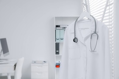 White doctor's gown and stethoscope hanging on rack in clinic. Space for text