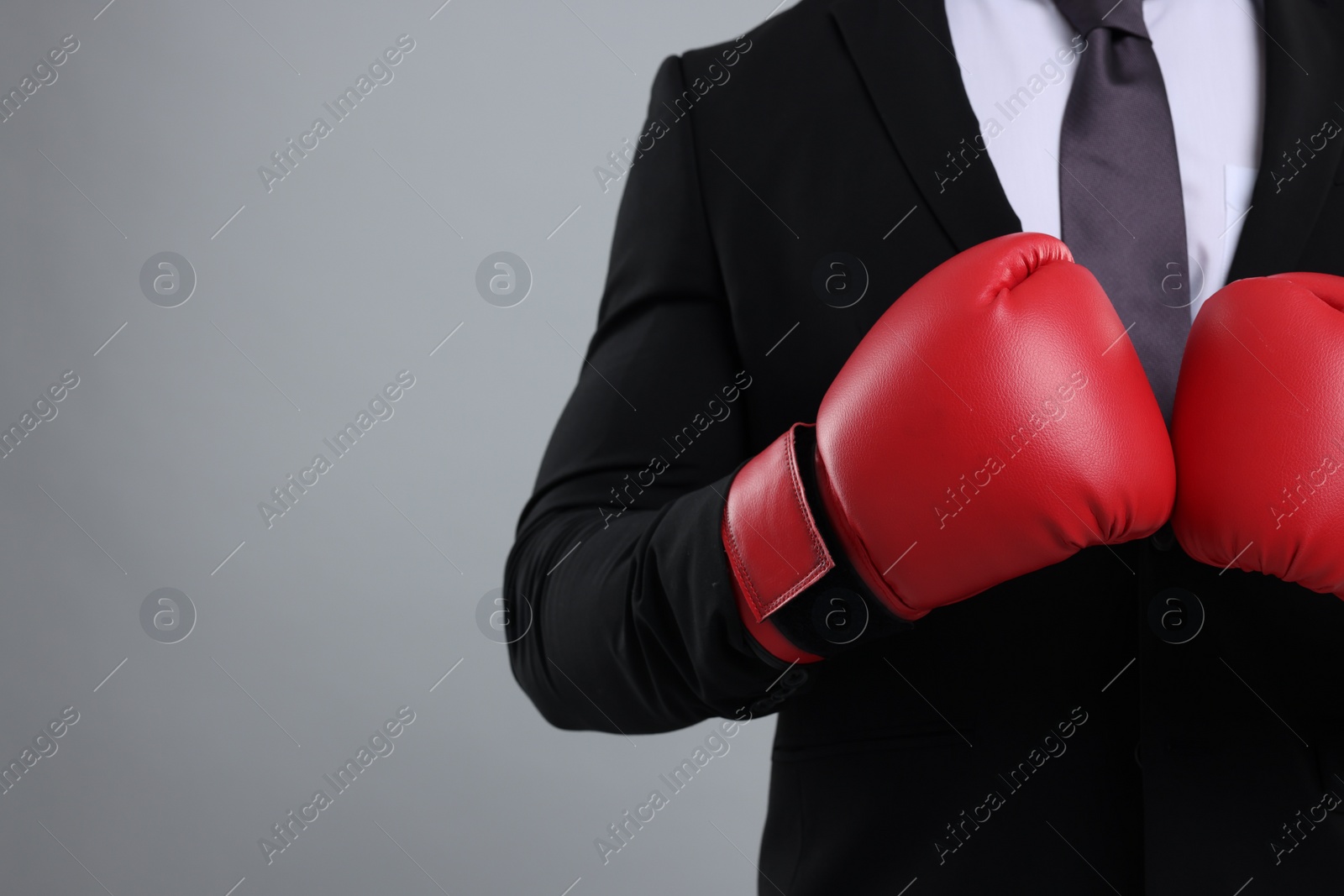 Photo of Businessman in suit wearing boxing gloves on grey background, closeup. Space for text