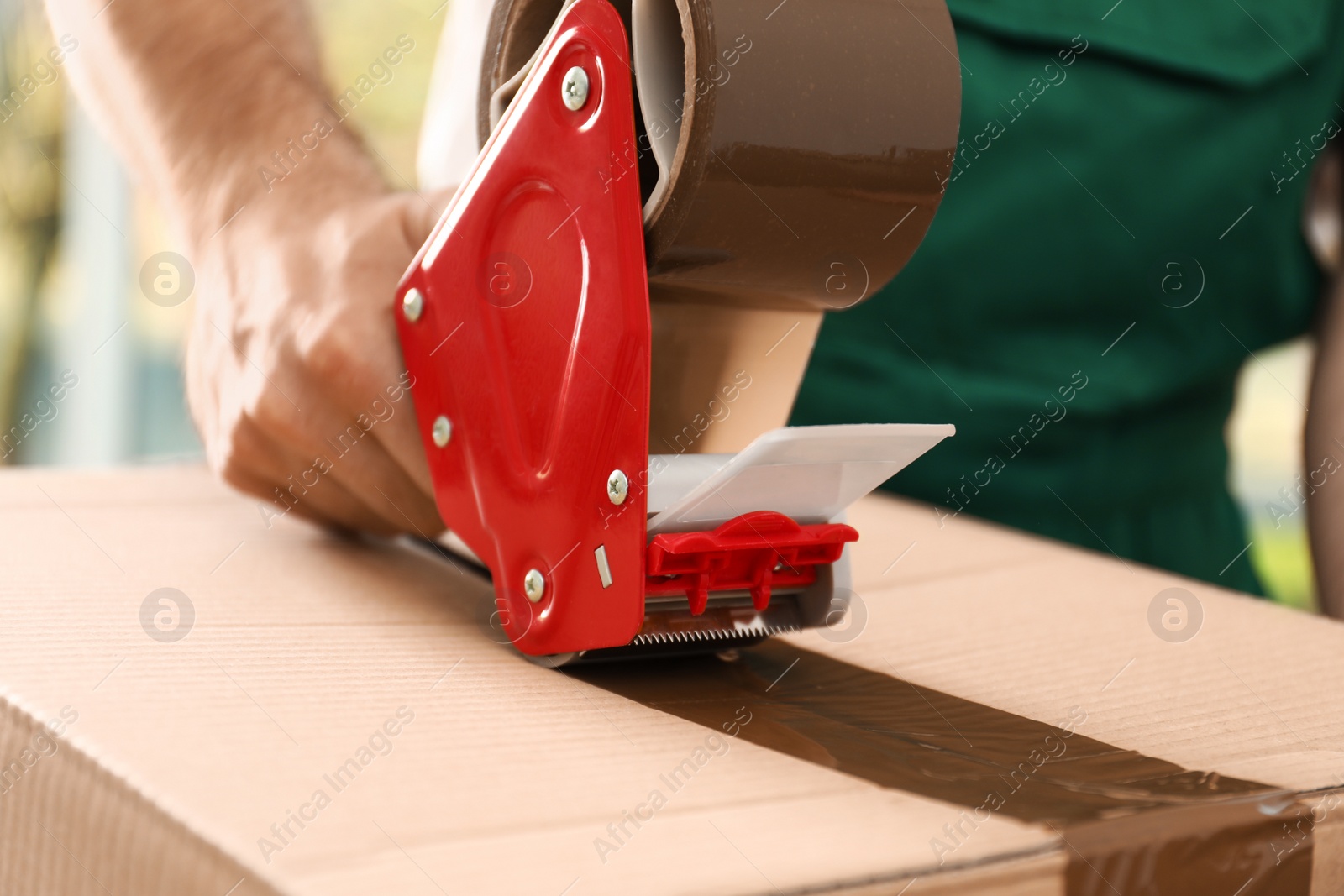 Photo of Man packing box with adhesive tape indoors, closeup. Moving service