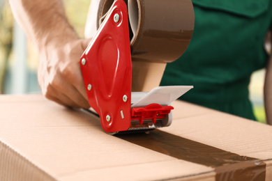 Photo of Man packing box with adhesive tape indoors, closeup. Moving service