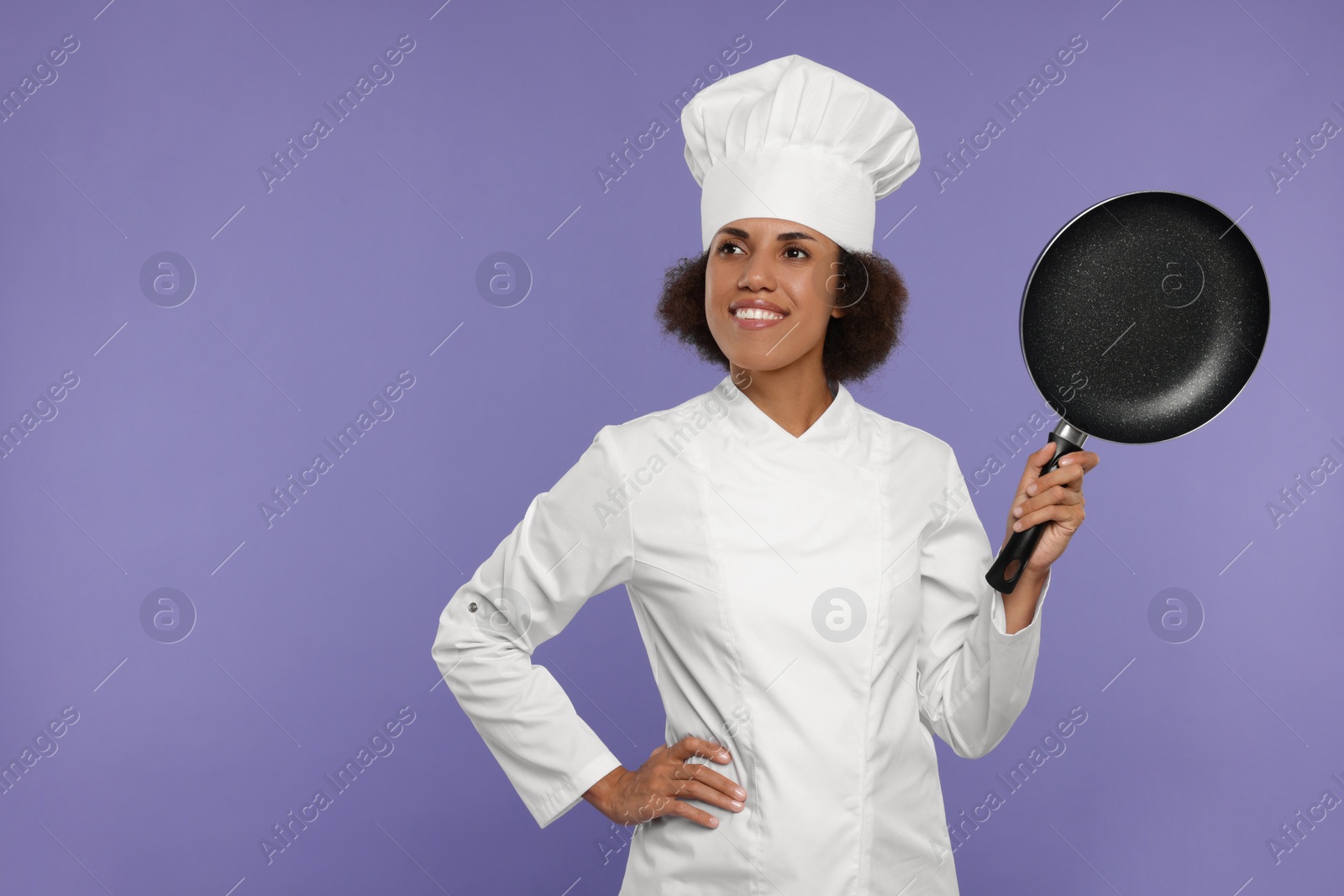 Photo of Happy female chef in uniform holding frying pan on purple background. Space for text