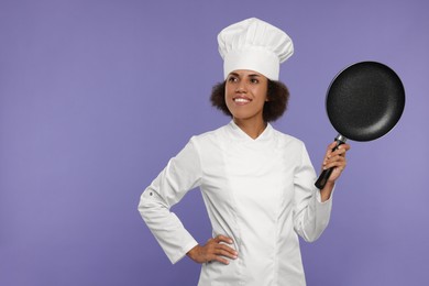 Photo of Happy female chef in uniform holding frying pan on purple background. Space for text