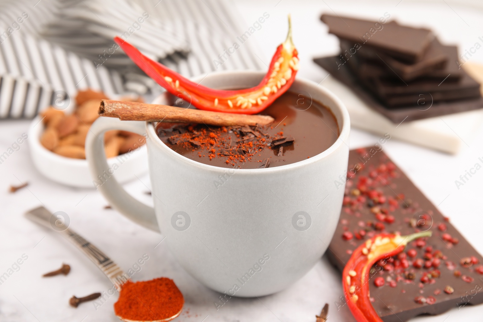 Photo of Cup of hot chocolate with chili pepper and cinnamon on white marble table, closeup