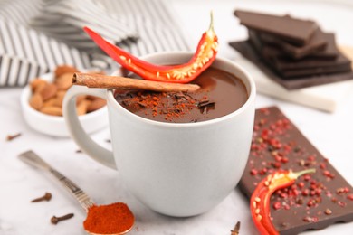 Photo of Cup of hot chocolate with chili pepper and cinnamon on white marble table, closeup