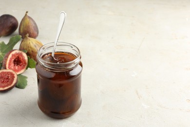 Photo of Jar of tasty sweet jam and fresh figs on light table, space for text