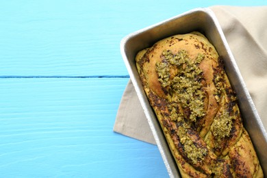 Photo of Freshly baked pesto bread in loaf pan on light blue wooden table, top view. Space for text