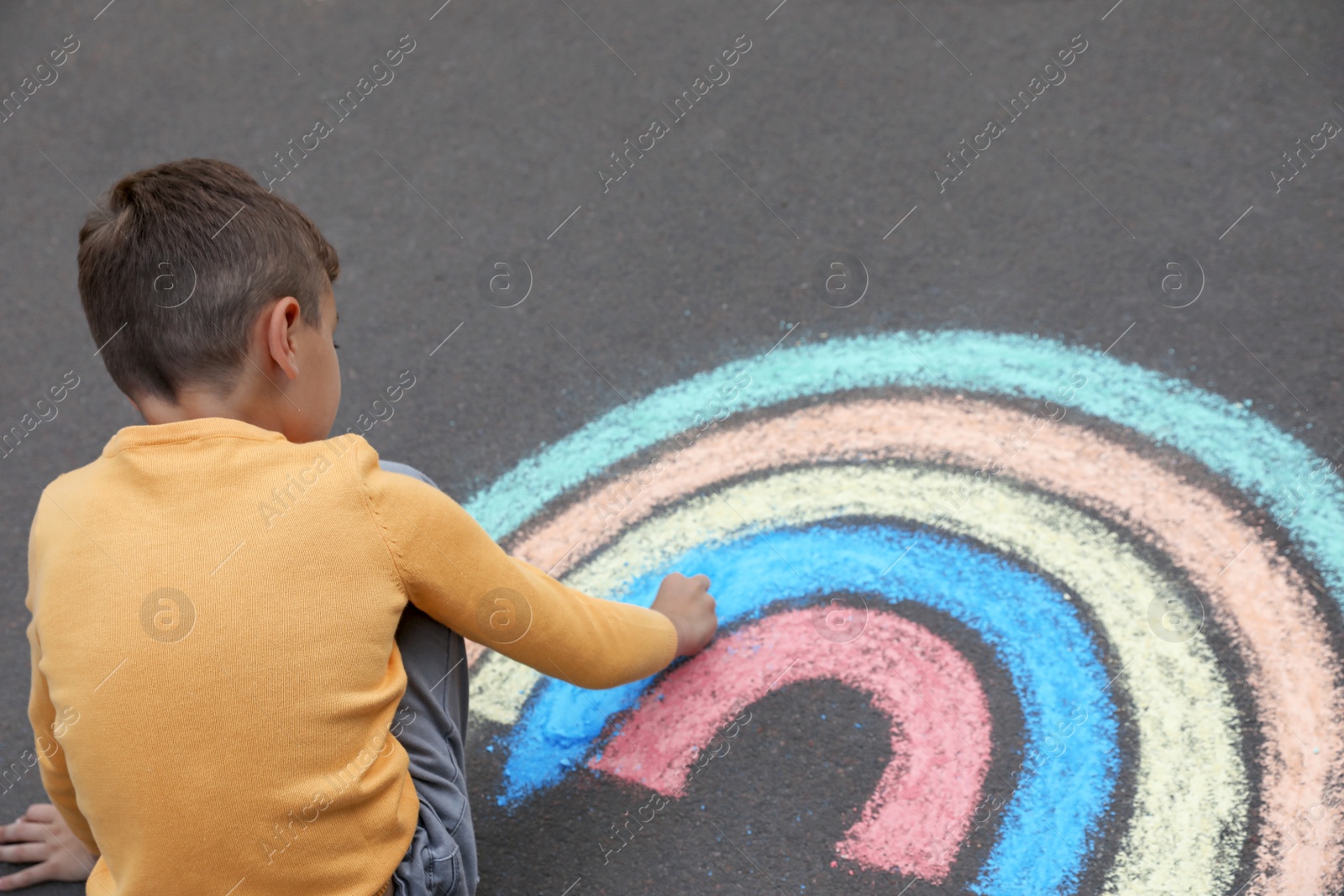 Photo of Child drawing rainbow with chalk on asphalt, above view