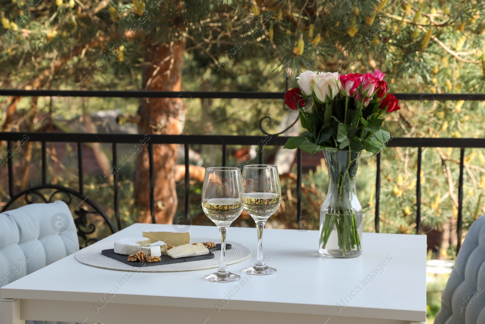 Photo of Beautiful roses, glasses of wine and snacks on white table at balcony