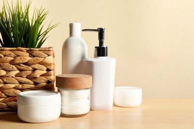 Different bath accessories and houseplant on wooden table against beige background, closeup. Space for text