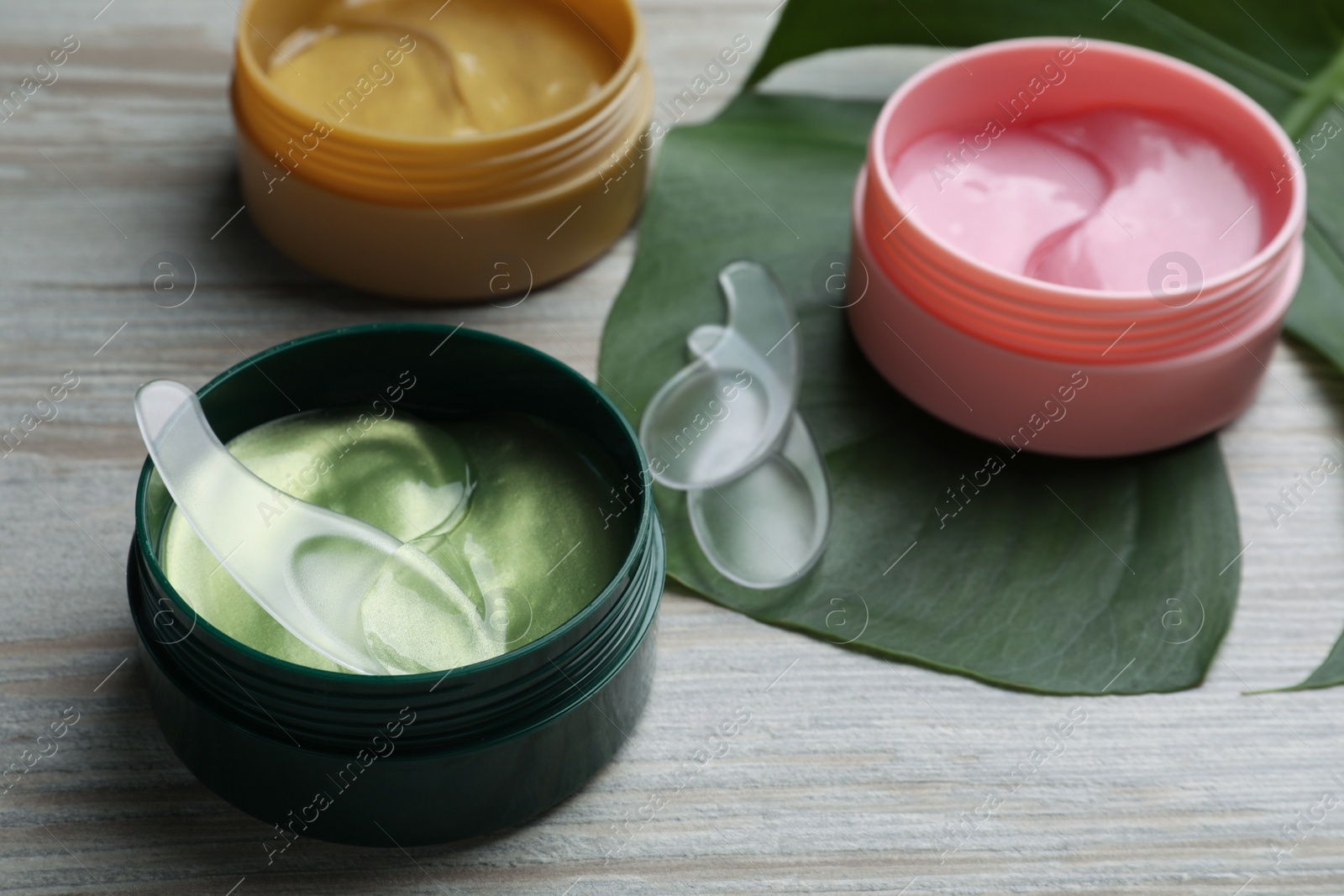 Photo of Packages of different under eye patches and tropical leaf on wooden table. Cosmetic product