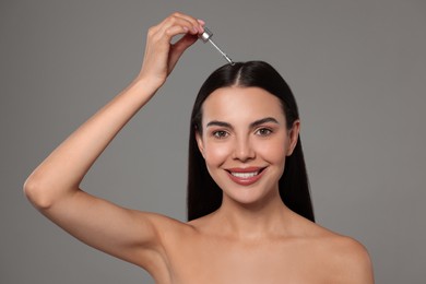 Photo of Beautiful woman applying hair serum on grey background. Cosmetic product