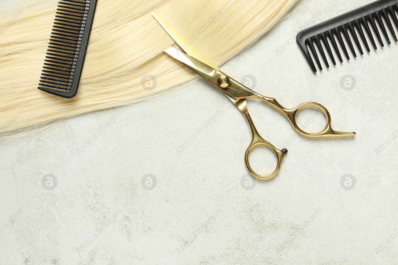 Photo of Professional hairdresser scissors and comb with blonde hair strand on grey table, top view. Space for text