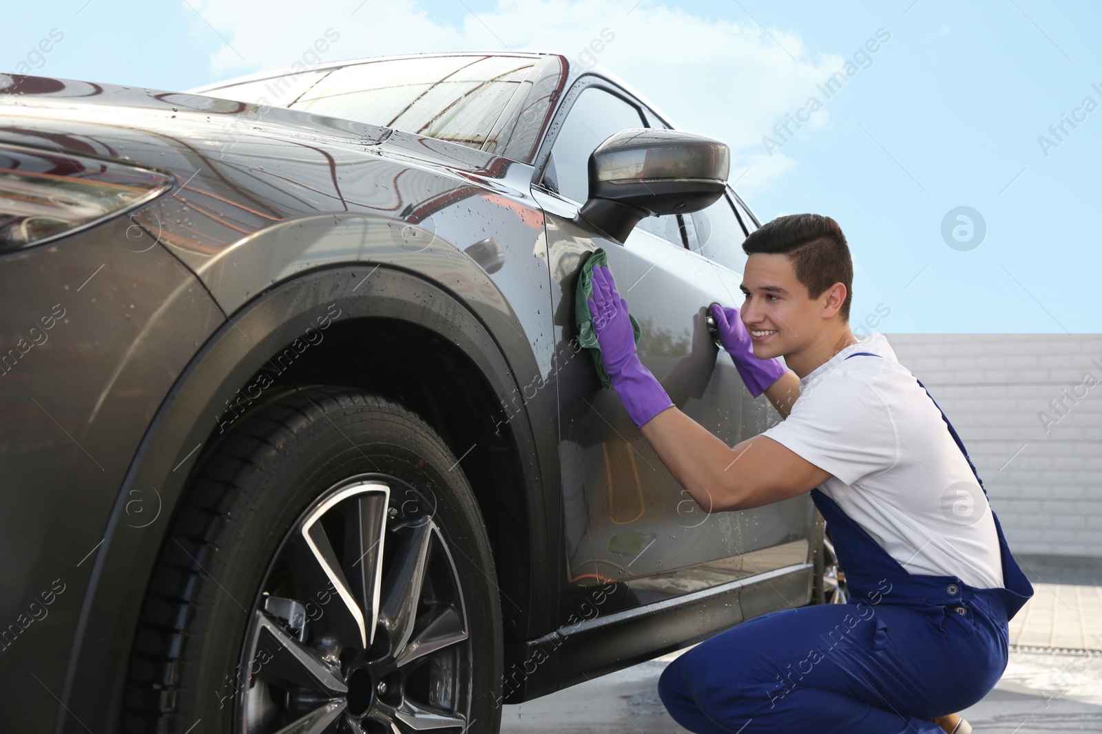 Photo of Male worker cleaning automobile door with rag at car wash