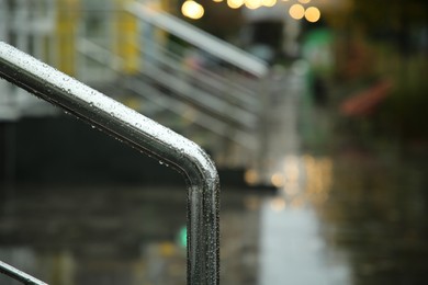 Photo of Metal handrail with raindrops outdoors, closeup. Space for text