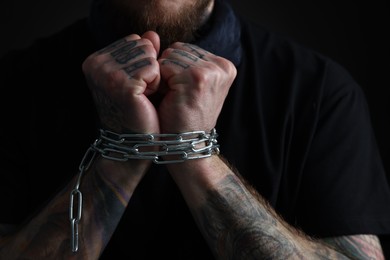 Photo of Man with chained hands on dark background, closeup. Hostage