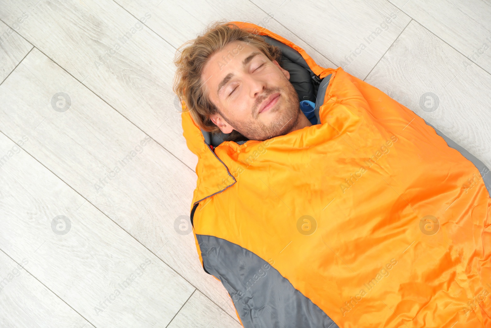 Photo of Young man in comfortable sleeping bag on floor, top view. Space for text