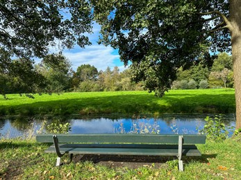 Photo of Wooden bench near pond in picturesque park