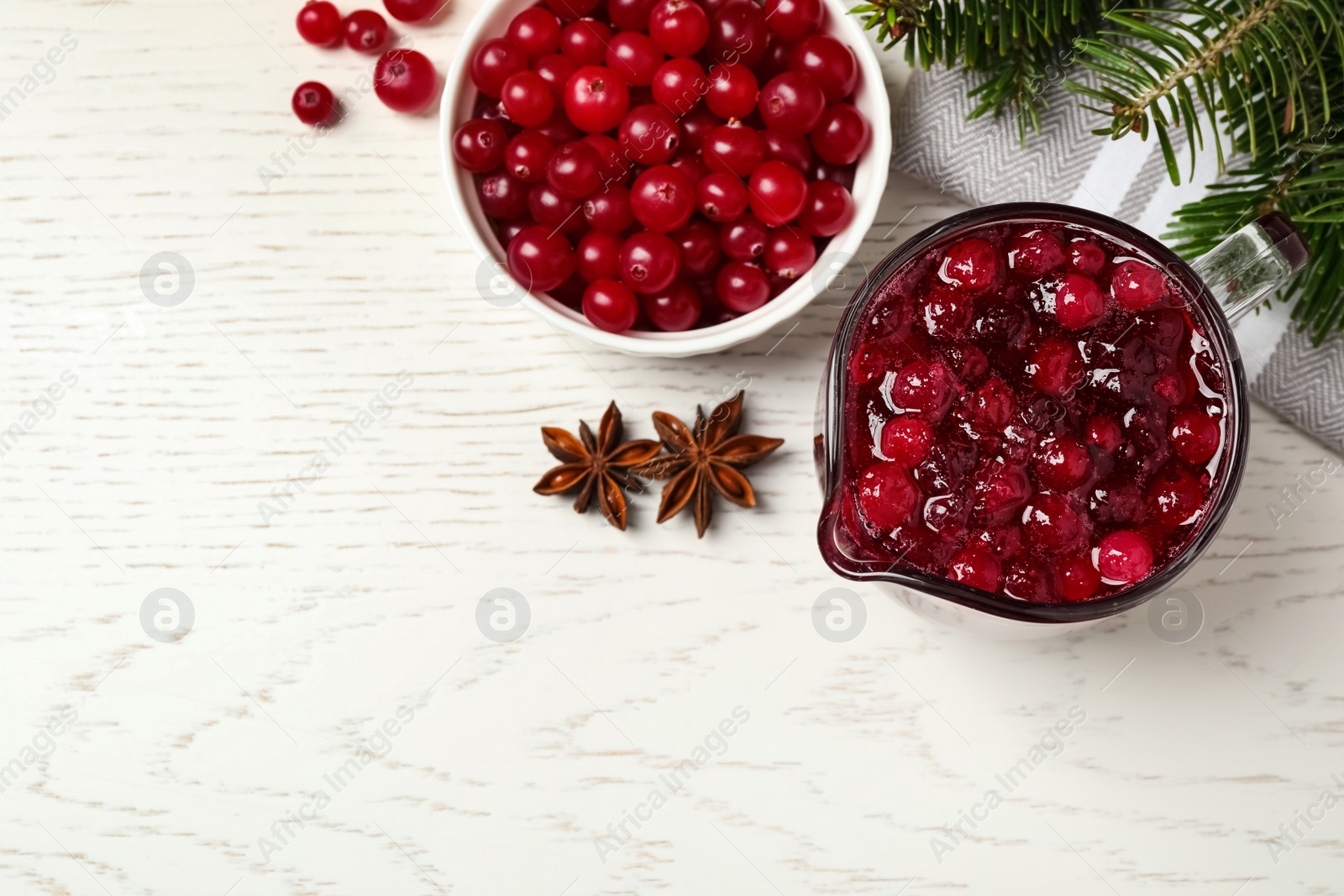 Photo of Flat lay composition with fresh cranberry sauce in pitcher on white wooden table, space for text