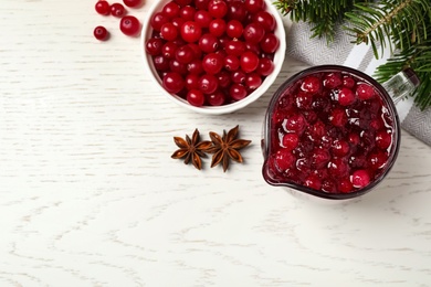 Photo of Flat lay composition with fresh cranberry sauce in pitcher on white wooden table, space for text