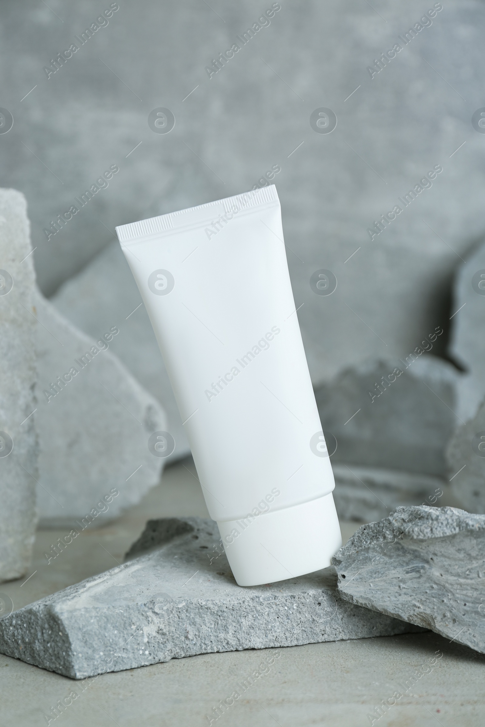 Photo of Tube of hand cream among stones on grey background. Mockup for design