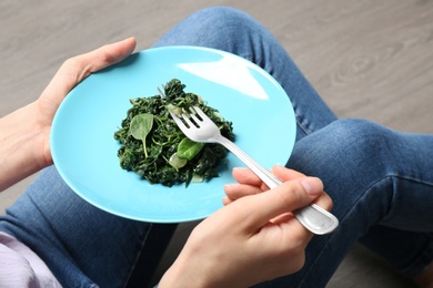 Photo of Young woman with tasty cooked spinach on wooden floor, closeup. Healthy food