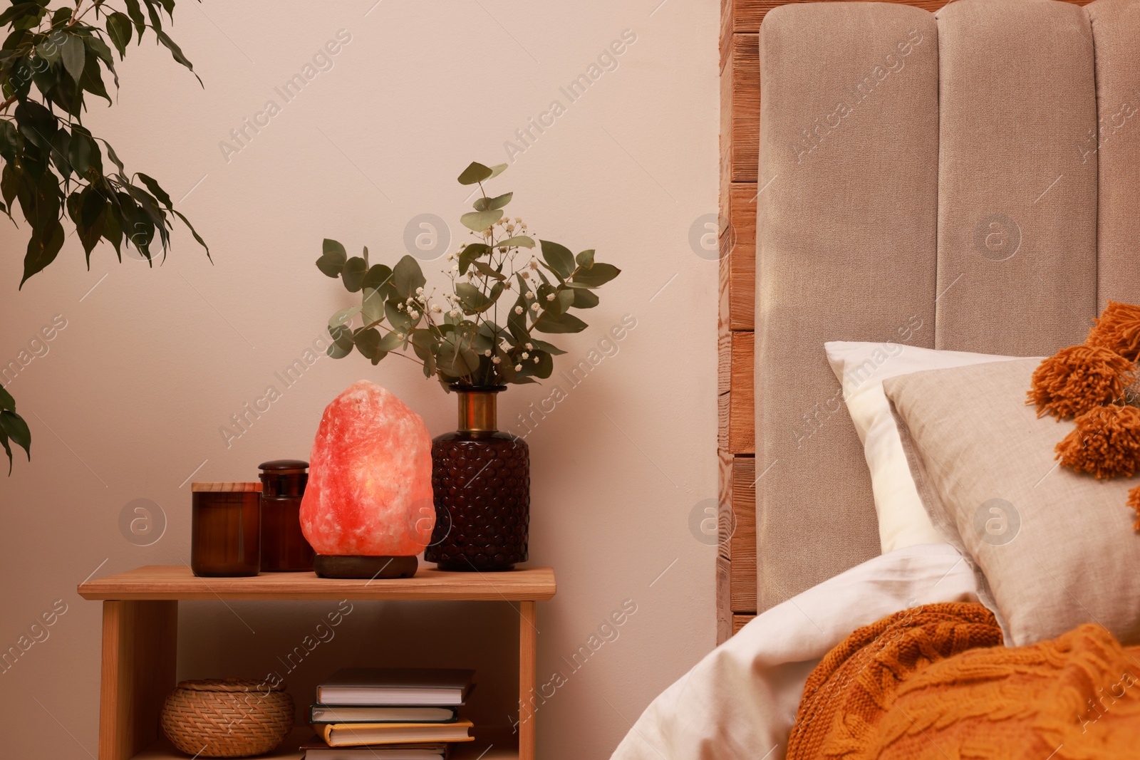 Photo of Beautiful Himalayan salt lamp and eucalyptus branches on nightstand in bedroom