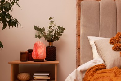 Beautiful Himalayan salt lamp and eucalyptus branches on nightstand in bedroom